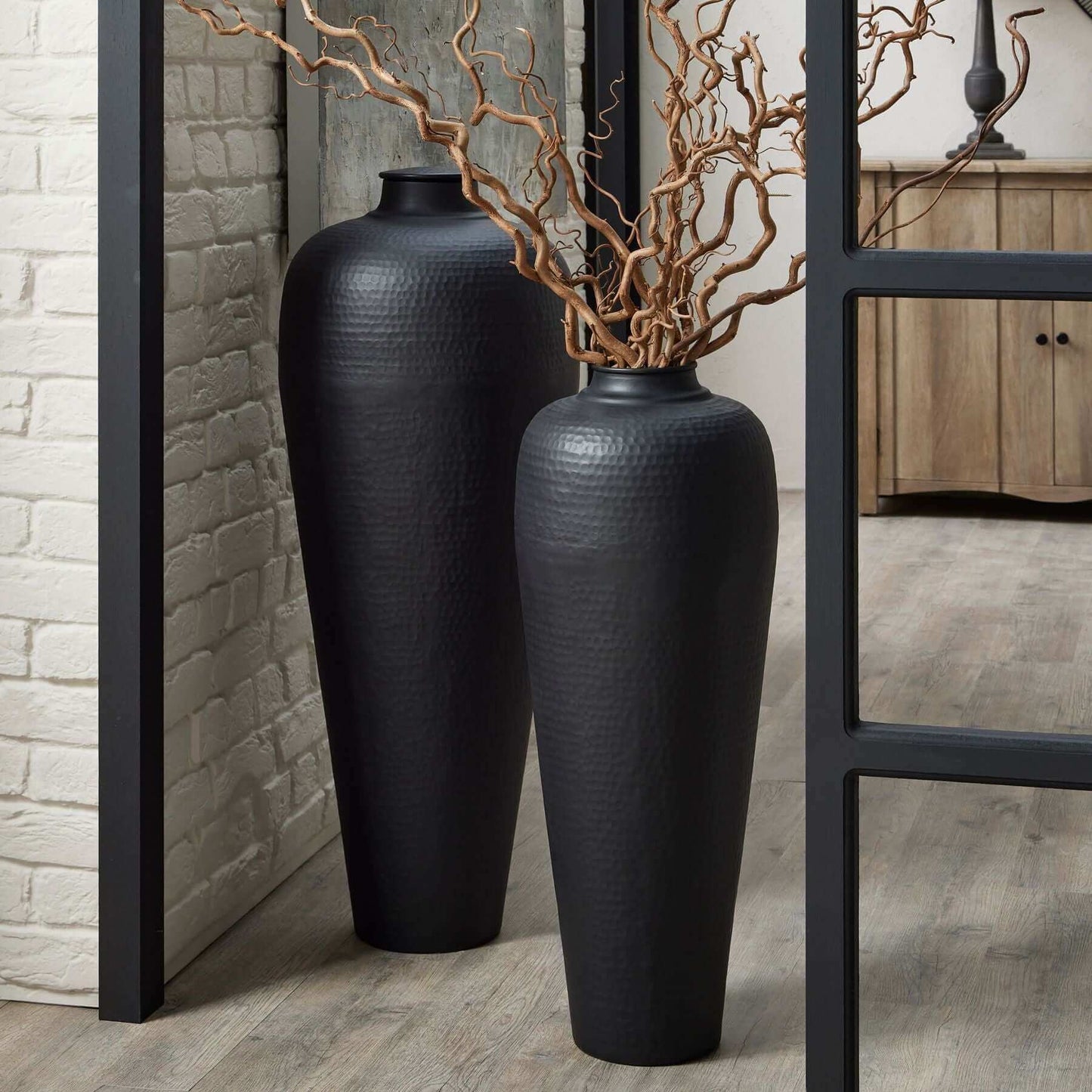 Large Hammered Vase | Description The meticulously crafted Large Hammered Vase in Matt Black comes with a lid and adds stylish charm to any space. Pair it with twisted hazel branches for a chic, floor-standing display. This modern piece makes a bold state