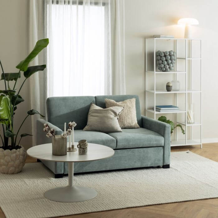 Modern living room with Newcastle Wall Unit in white rough powder-coated steel frame and asymmetrical shelves, beside a green sofa and coffee table.